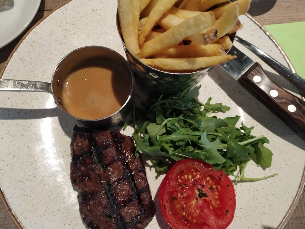 Rump steak with peppercorn sauce, fries, rocket salad and grilled tomato as the main, served on a plate