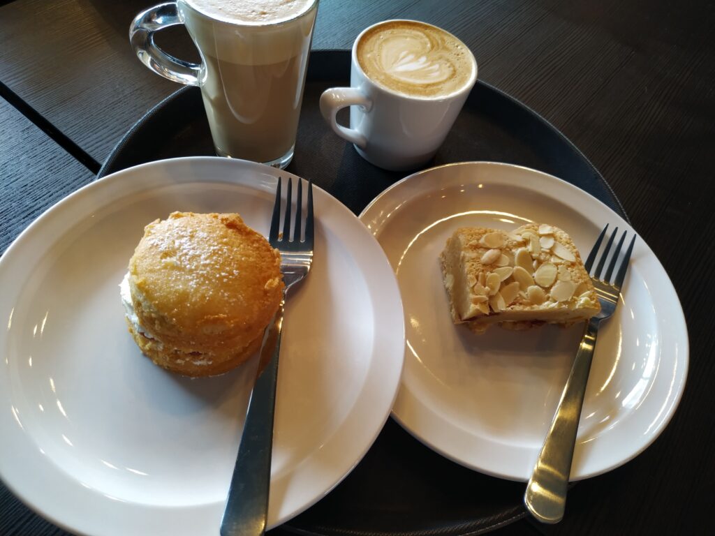 Latte & flat white with a victoria sponge cake &  bakewell blondie served on plates and a tray